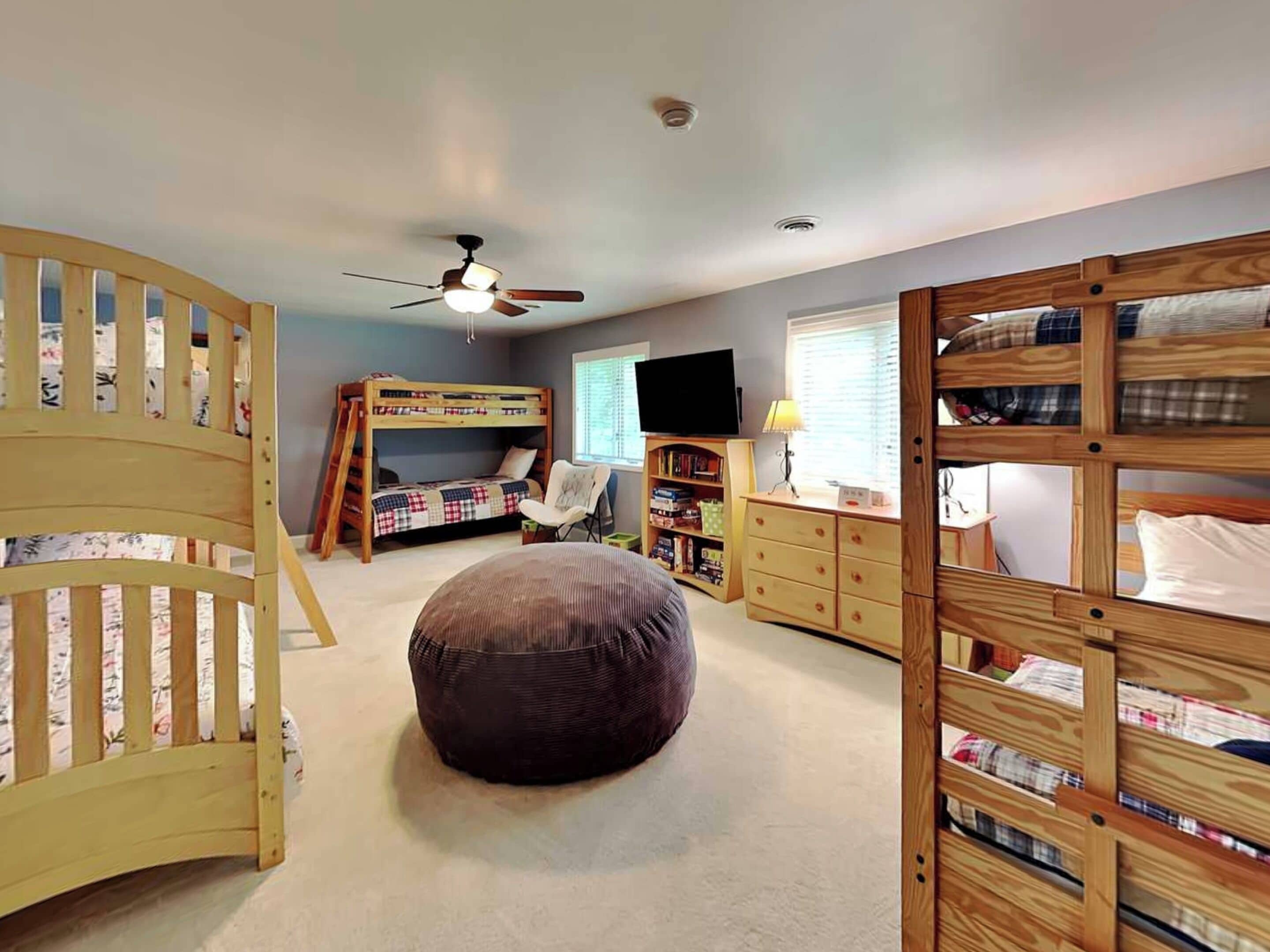 A child's bedroom with bunk beds, a ceiling fan, a TV, and a bookshelf.