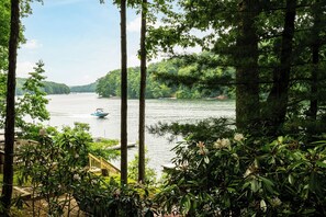 A serene lakeside view with a boat on the water, surrounded by lush greenery and a wooden deck. - Loch Haven by Taylor Made Deep Creek (McHenry)