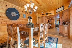 Cozy cabin interior with a dining area, kitchen, and a chandelier.