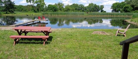 A lakeside picnic area with picnic tables and chairs, a dock, and a grassy field.
