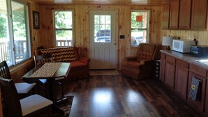 A cozy cabin interior with a dining area, a kitchen with wooden cabinets, and a large window providing natural light.