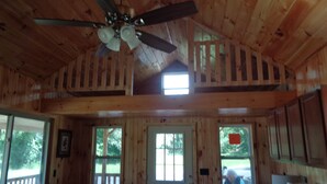 A cabin with a wooden interior, a ceiling fan, a front door, and a view of the outside.