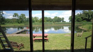 A view from inside a building looking out to a grassy area with a pond, a picnic table, and a wooden deck.