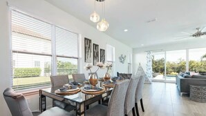 A modern dining area with a glass table, grey upholstered chairs, and decorative plates. - Disney Dreams: 6BR/6BA, Pool, Spa, Golf, Star Wars Cinema, Avatar & Princesses! (Kissimmee)