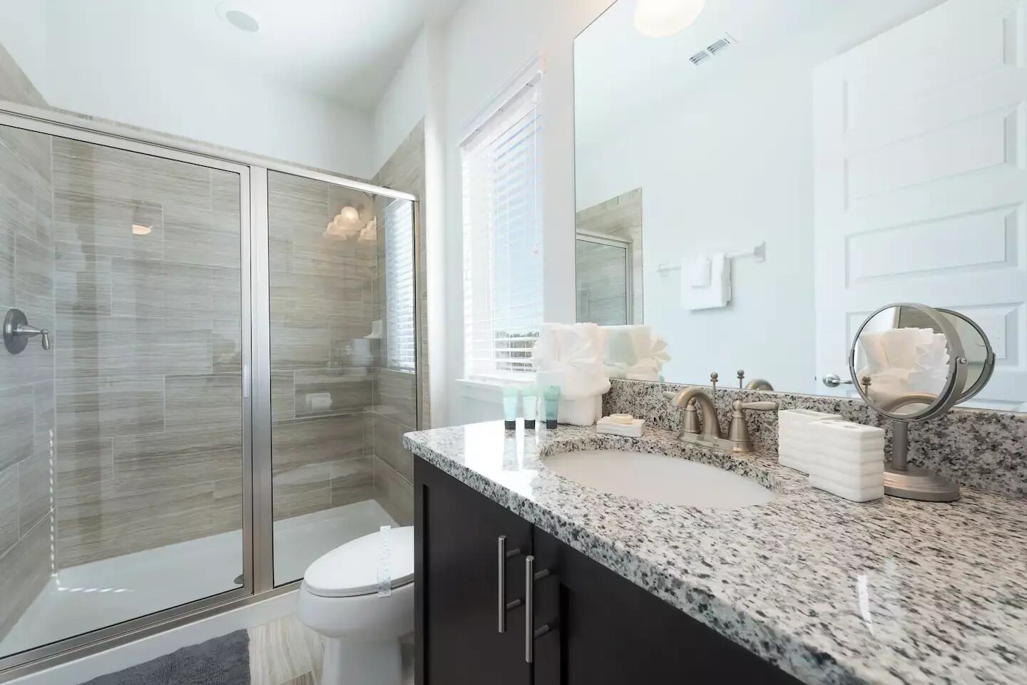 Une salle de bain moderne dotée d’une douche à parois de verre, d’un meuble-lavabo avec un plan de travail en granit et d’un grand miroir.