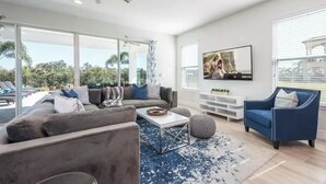A modern living room with a grey sofa, a blue armchair, and a coffee table. - Disney Dreams: 6BR/6BA, Pool, Spa, Golf, Star Wars Cinema, Avatar & Princesses! (Kissimmee)
