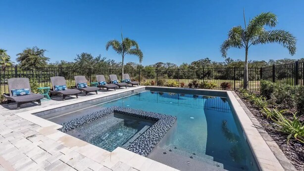 A swimming pool with lounge chairs and a hot tub, surrounded by palm trees and a fence. - Disney Dreams: 6BR/6BA, Pool, Spa, Golf, Star Wars Cinema, Avatar & Princesses! (Kissimmee)