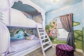 Habitación con literas, un mural y un reposapiés morado.