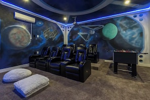 Una habitación con un mural con temática espacial, una mesa de fútbol de mesa y varias sillas reclinables.