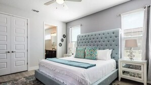 A bedroom with a large bed, a ceiling fan, a nightstand with a lamp, and a door. - Disney Dreams: 6BR/6BA, Pool, Spa, Golf, Star Wars Cinema, Avatar & Princesses! (Kissimmee)