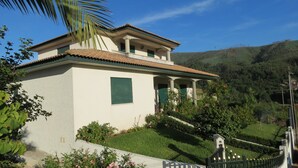 A two-story house with a tiled roof, green shutters, and a covered porch. - Refúgio de Selores (Oliveira de Azeméis)