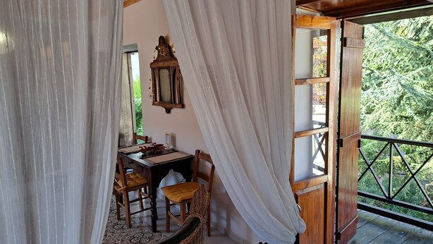 Zona pranzo con tavolo e sedie, un armadietto in legno e vista sul verde attraverso una finestra con tende.