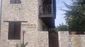 Un edificio in pietra con una porta in legno e persiane, un balcone con ringhiera in metallo e una pianta in vaso in primo piano.