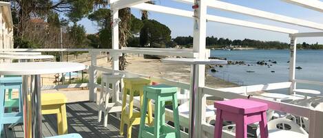 A deck with colorful stools and tables overlooking a beach.