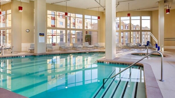 An indoor swimming pool with clear water, sunlit by large windows, and lounge chairs around the pool area.