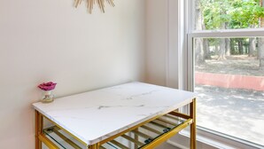Ein weißer Marmor-Tisch mit goldener Umrandung, nahe einem Fenster mit Blick auf Bäume und einen roten Zaun.
