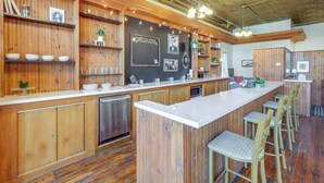 Eine moderne Küche mit Holdekor, einer weißen Arbeitsplatte und Barhocker. Regale mit Geschirr und eine Tafel mit freundlicher Begrüßung.