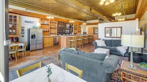 Ein großzügiger Wohnbereich mit grauem Sofa, einem Holzespeisetisch und einer Küchenzeile, die einen Edelstahlkühlschrank und Holzschränke beinhaltet.