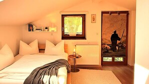 Un dormitorio con cama, mesita de noche, lámpara, ventana y puerta decorada con un cuadro.