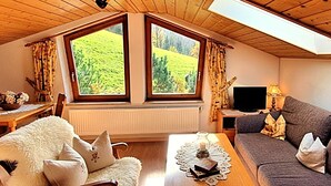 Una sala de estar acogedora con techo de madera, un sofá, una mesa con un jarrón y flores, y una ventana con cortinas.