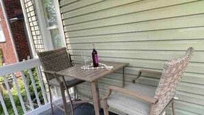 Een overdekte terras met een houten tafel en twee rieten stoelen.