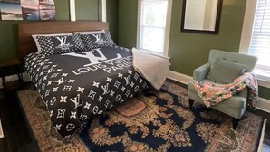 Een slaapkamer met een bed, een plafondventilator, een stoel en een groot vloerkleed.