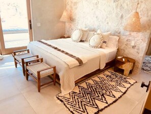 Relax in this serene bedroom with a large bed, a wooden bench, and a patterned rug.