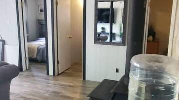 A room with a wooden floor, a grey sofa, a black heater, and a water dispenser.