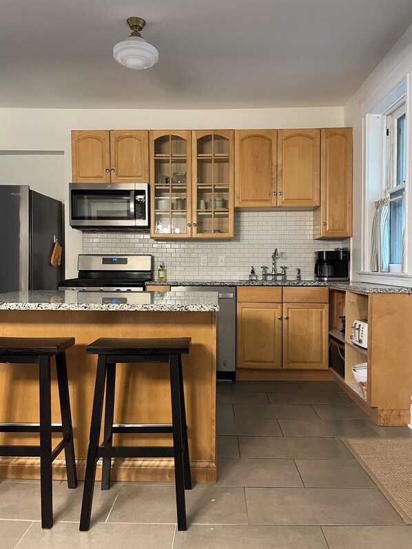 A modern kitchen with wooden cabinets, a stainless steel refrigerator, a microwave, a dishwasher, and a granite countertop.
