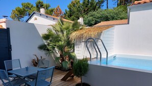 Un espace piscine doté d’une terrasse en bois, de chaises en métal, d’une petite table et d’un mur blanc.