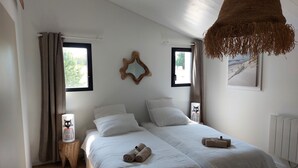 Une chambre avec deux lits, une grande fenêtre, un luminaire suspendu et un radiateur.