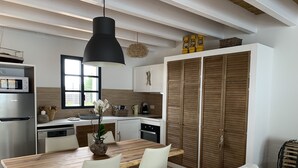 Une cuisine moderne avec une table à manger en bois, des chaises blanches et un luminaire suspendu noir.