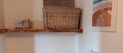 A room with a wooden cabinet with drawers, a wicker basket on a shelf, a radiator, and a framed picture on the wall.