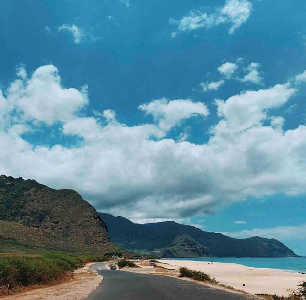 A coastal road leading to a beach with mountains in the background.