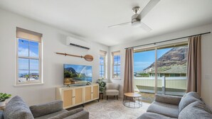 Un vaste salon doté d’une grande fenêtre donnant sur un paysage montagneux, d’un ventilateur de plafond et d’un téléviseur posé sur un meuble en bois.