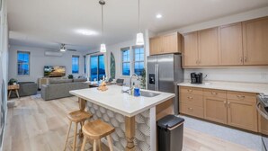 Une cuisine moderne dotée d’un îlot central, de tabourets en bois, d’un réfrigérateur en acier inoxydable et d’armoires en bois.