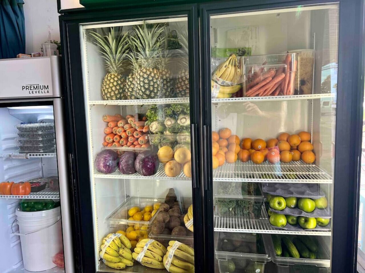 Un présentoir réfrigéré contenant divers fruits et légumes, notamment des ananas, des bananes, des oranges et des pommes.