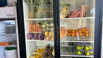 Un présentoir réfrigéré contenant divers fruits et légumes, notamment des ananas, des bananes, des oranges et des pommes.