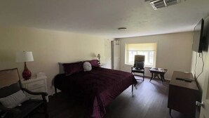 Un dormitorio con cama, mesitas de noche, una silla, escritorio y televisor.
