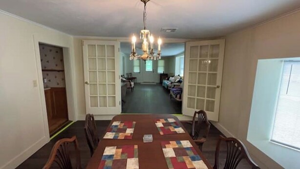 Comedor con una mesa lista para cuatro, una araña y vista a una sala de estar a través de una puerta abierta.