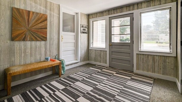 Een hal met een houten bankje, een getextureerd vloerkleed en een bord waarop staat: RELAX AND LUMIND.
