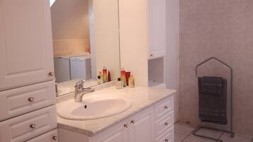 Une salle de bain avec un grand miroir, des meubles blancs, un lavabo et un porte-serviettes.