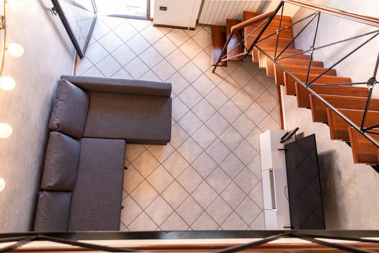 Ein modernes Interieur mit einer Holztreppe, einem grauen Ecksofa und einem gefliesten Boden.