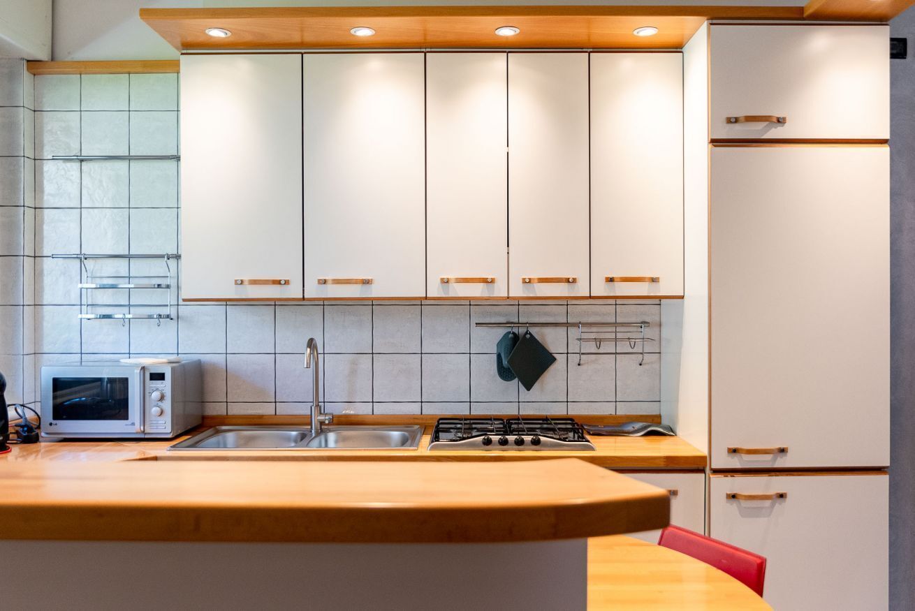 Una cocina moderna con armarios blancos, un lavamanos de acero inoxidable, una estufa a gas y un microondas.