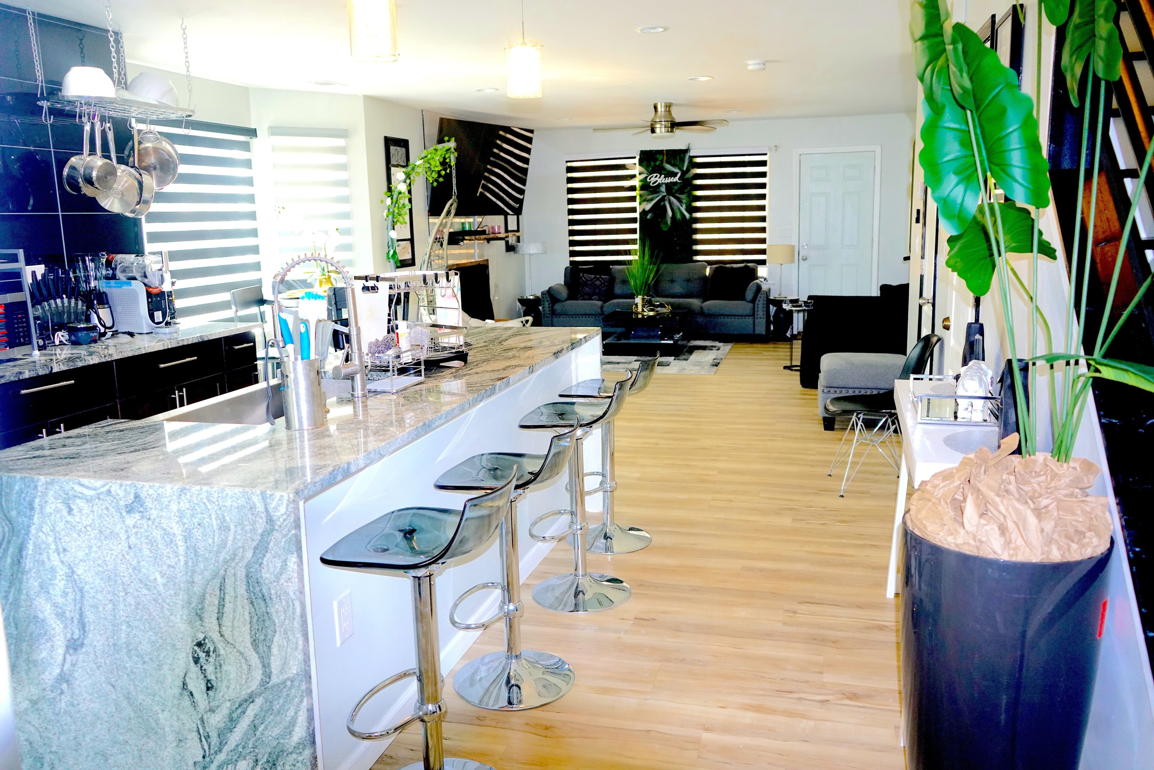 A modern kitchen with a marble island, bar stools, and a large potted plant.