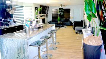 A modern kitchen with a marble island, bar stools, and a large potted plant.