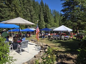 Guests can enjoy outdoor events in a serene grassy area surrounded by trees, with seating and tables available.