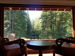 Enjoy a peaceful retreat with a forest view from the large window, featuring a round table and two chairs with intricate details.