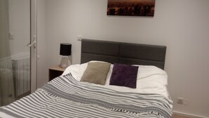 Ein Schlafzimmer mit Bett, Nachttisch, Lampe, einem Bild und einer Tür.
