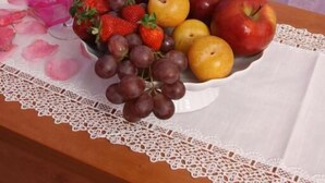 A neatly arranged fruit and champagne set on a table with a lace doily, a wooden nightstand with a lamp, and a bed with a white bedspread in a room with purple walls. - B&B A Casa di Giordy (Castro)